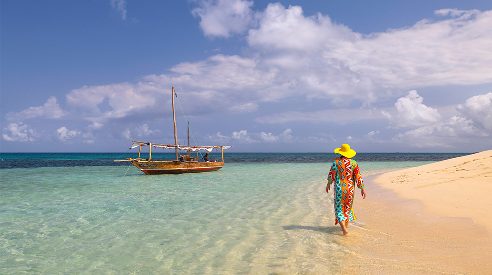 One tourist walking on the beach during a sunny day, with a boat in foreground, Zanzibar, Tanzania, Africa